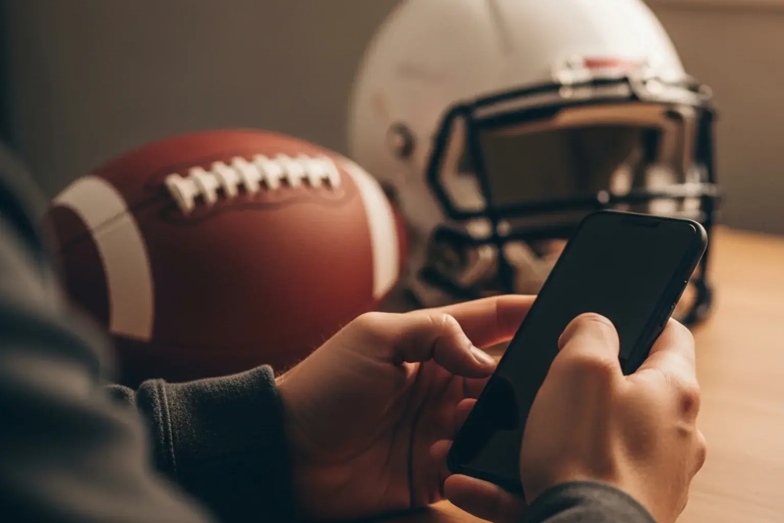 Hands holding a smartphone with an American football and helmet blurred in the background
